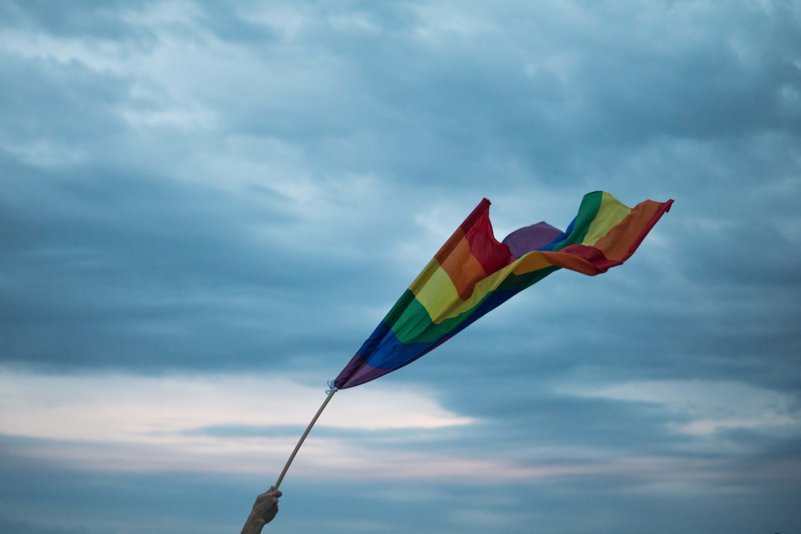 A hand holding an LGBTQ Pride flag. (Image: 
Yannis Papanastasopoulos/Unsplash)